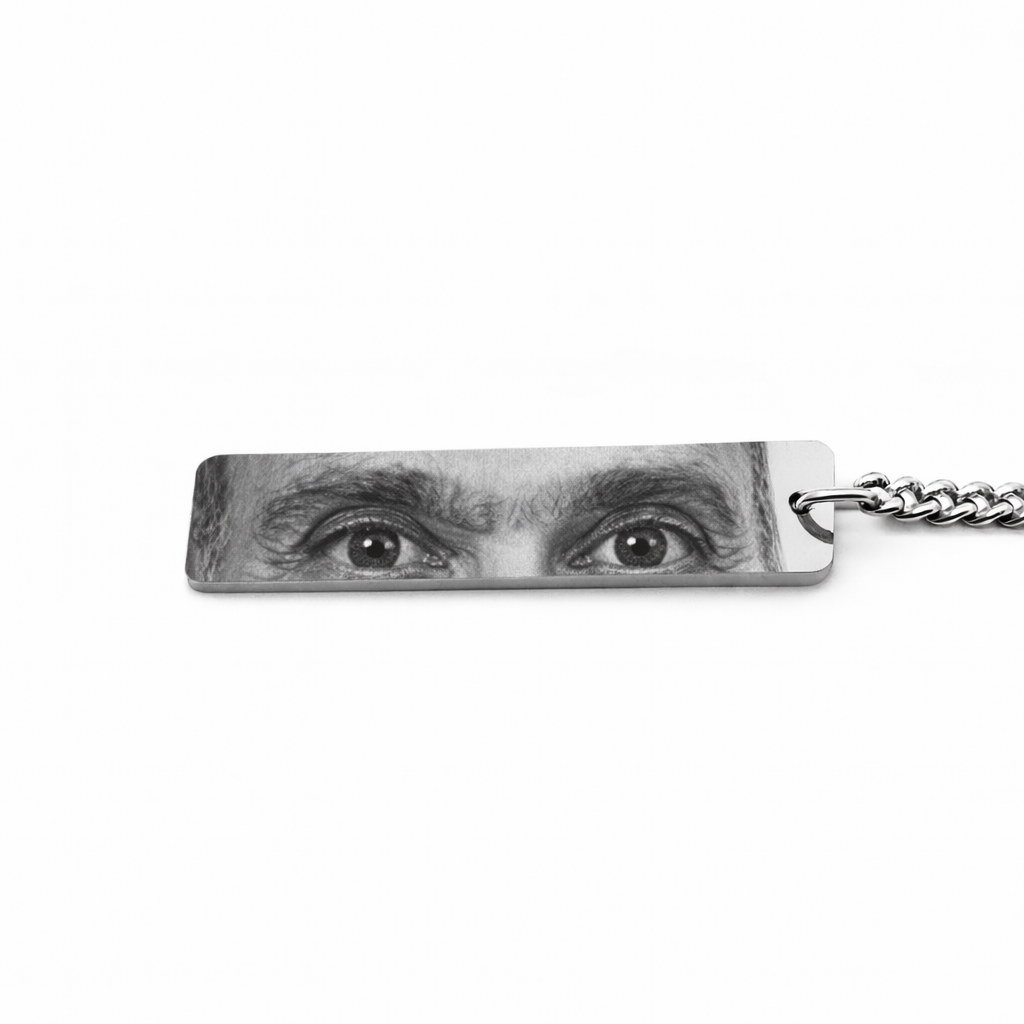 a silver keychain pendant featuring the eyes of an elderly man who has passed in greyscale