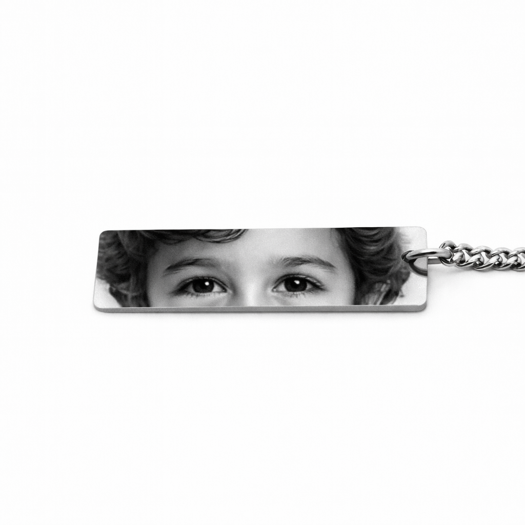 a silver keychain pendant featuring the eyes of a young boy in a greyscale tone