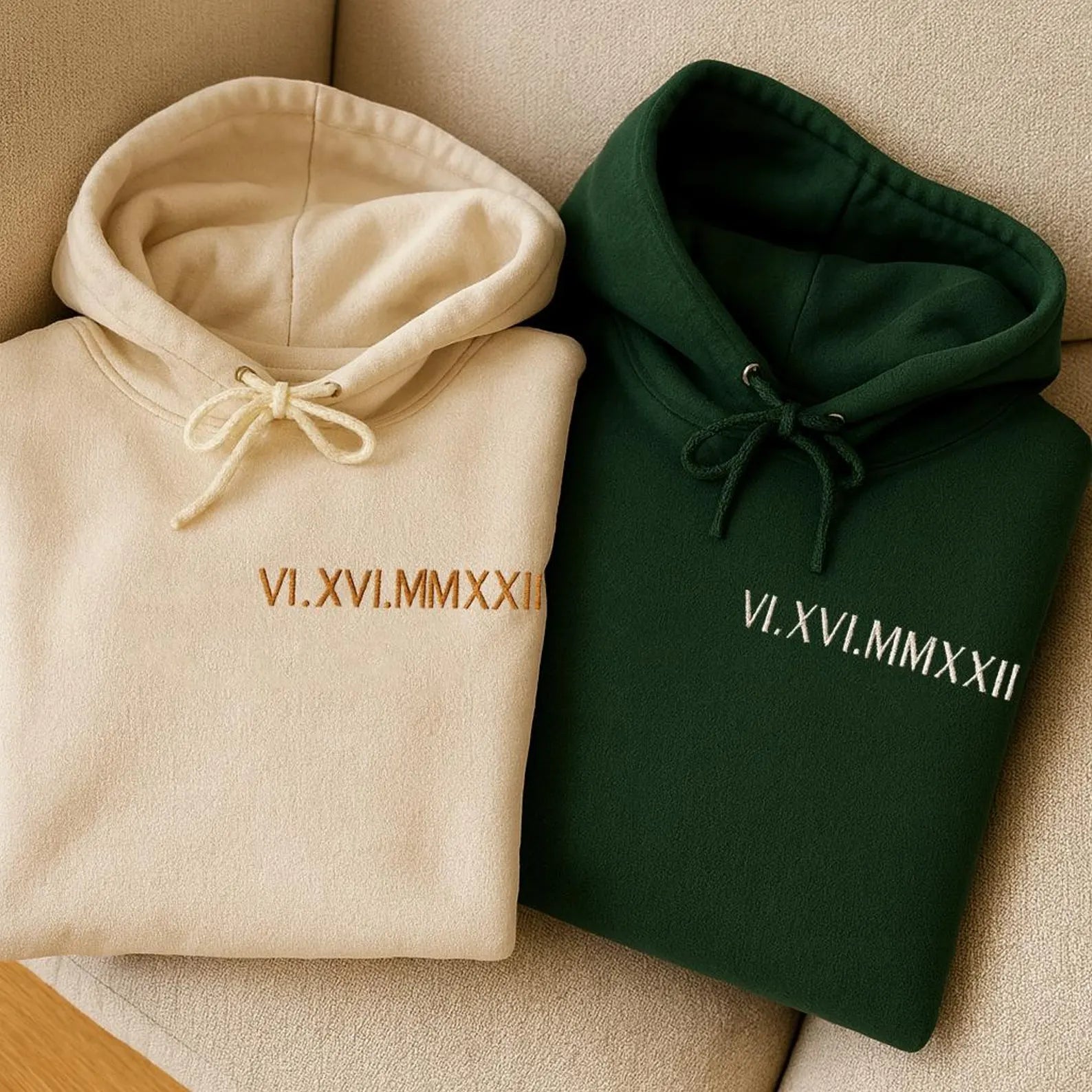 a cream-colored hoodie and a green hoodie folded neatly together and each featuring the same set of roman numeral embroidery