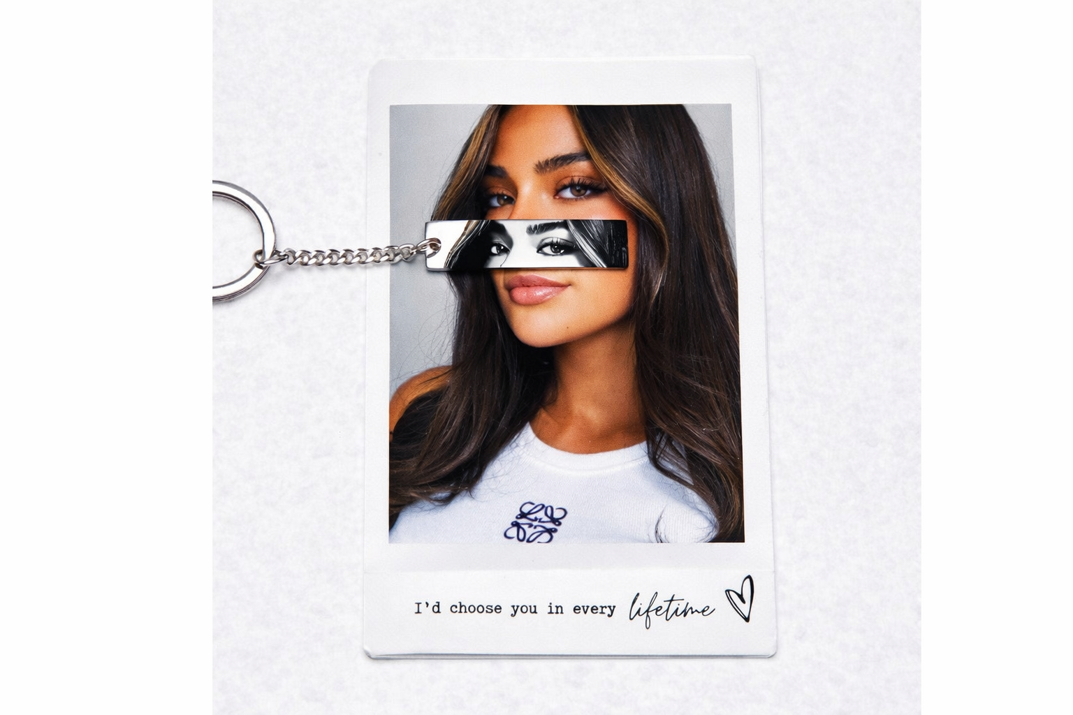 a silver keychain with a black and grey image of the eyes of a woman, who is featured from the neck up on a polaroid laid beneath the keychain. the bottom of the polaroid includes the text-- "I'd choose you in every lifetime"