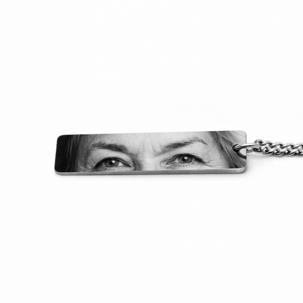 a silver keychain pendant featuring the eyes of an elderly woman who has passed in a greyscale tone