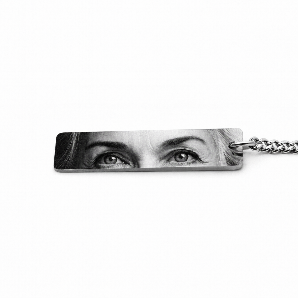 a silver keychain pendant featuring the eyes of an elderly woman who has passed in a greyscale tone