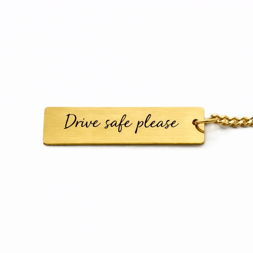 the back of a gold keychain pendant which features custom text in a casual script font, reads "drive safe please"