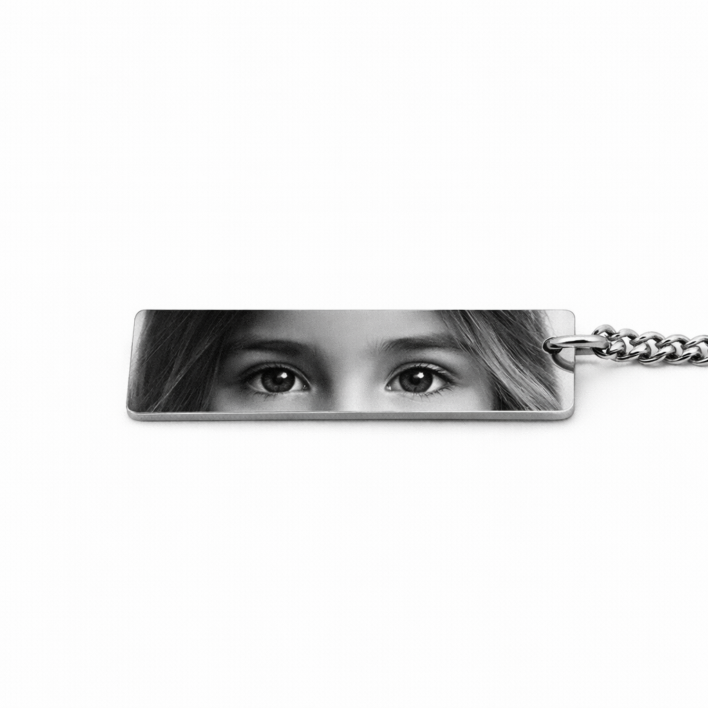 a silver keychain featuring the eyes of a child in greyscale