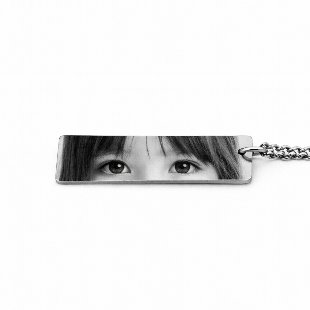 a silver keychain pendant featuring the eyes of a young girl in a greyscale tone