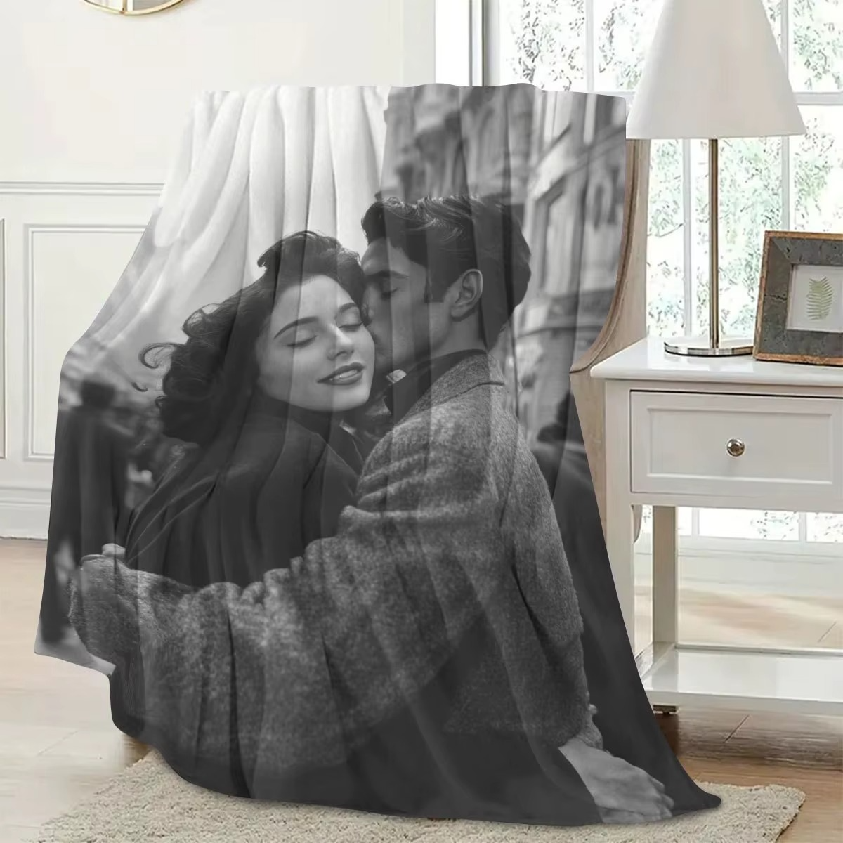 a blanket printed with a greyscale photo of a couple embracing is draped over a brown chair next to a white side table