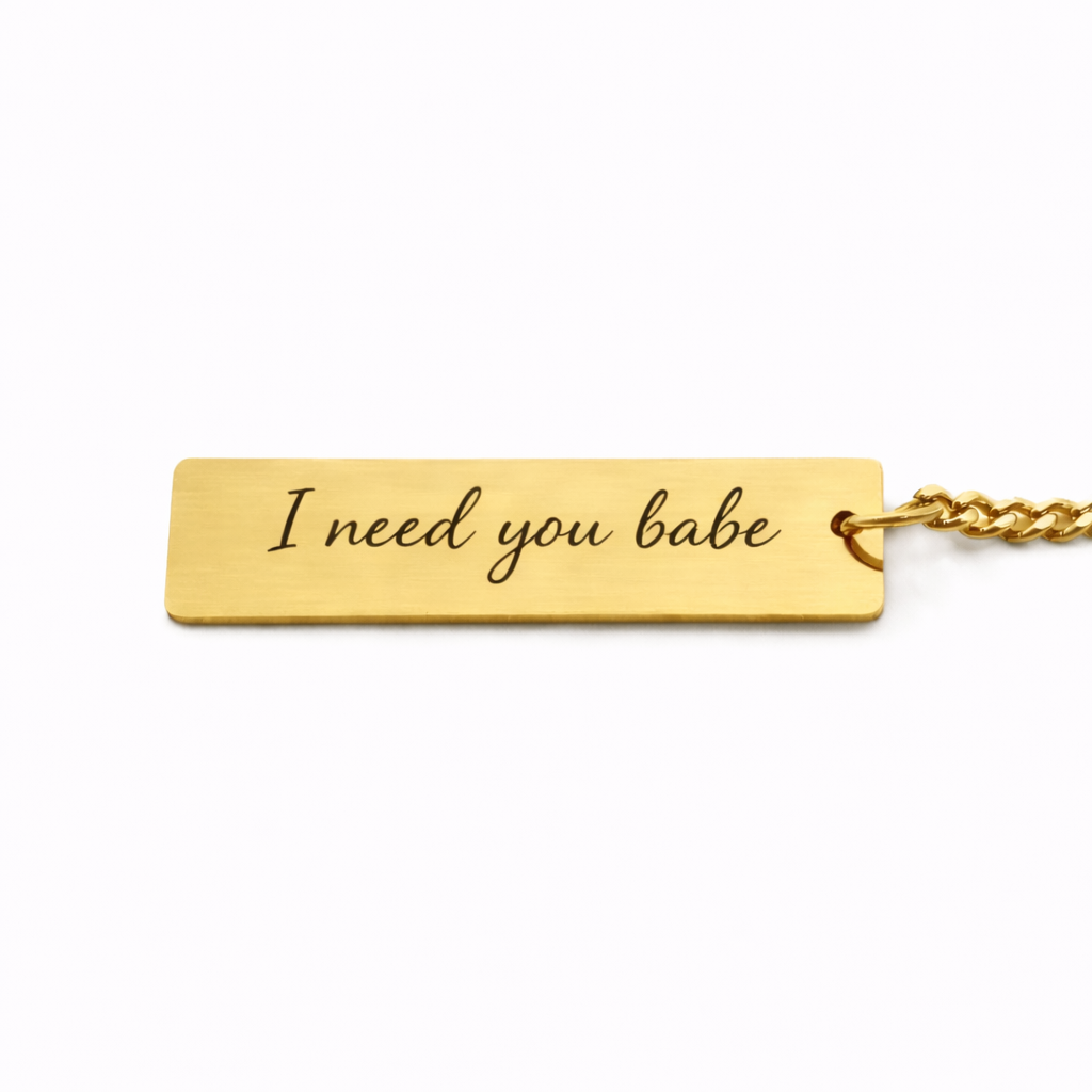 the back of a gold keychain pendant which features custom text in a casual script font, reads "i need you babe"