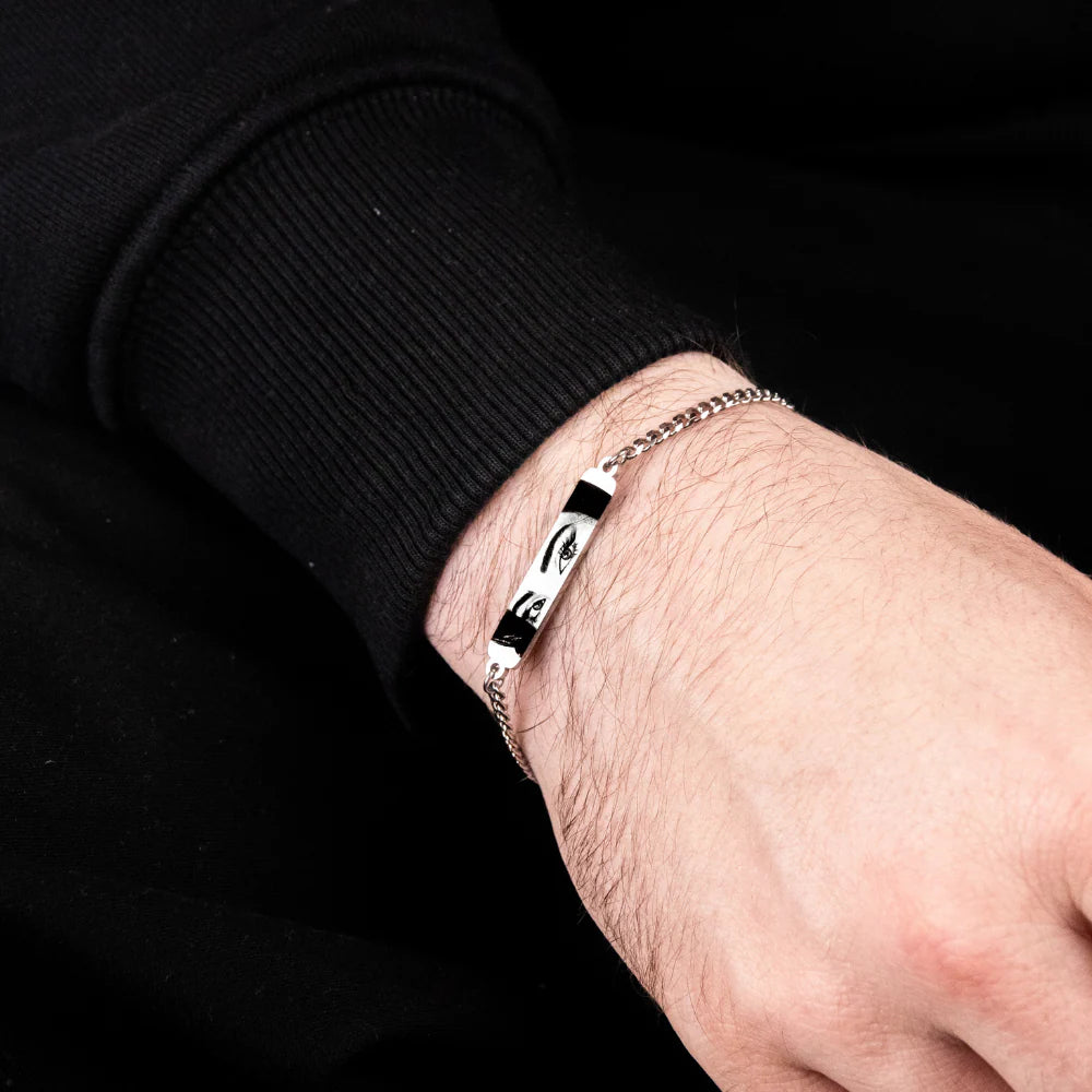 closeup image of a silver bracelet featuring a print of a woman's eyes in black and white on a man's wrist