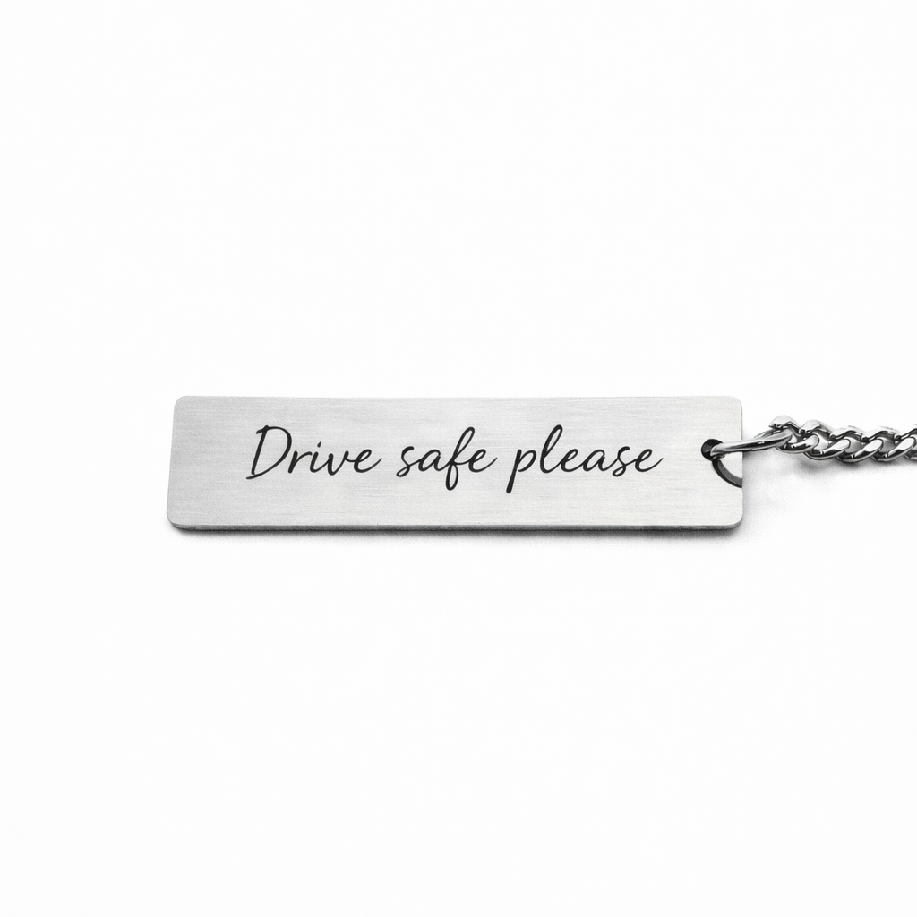 a silver keychain pendant with custom writing in a casual script font that reads "drive safe please"