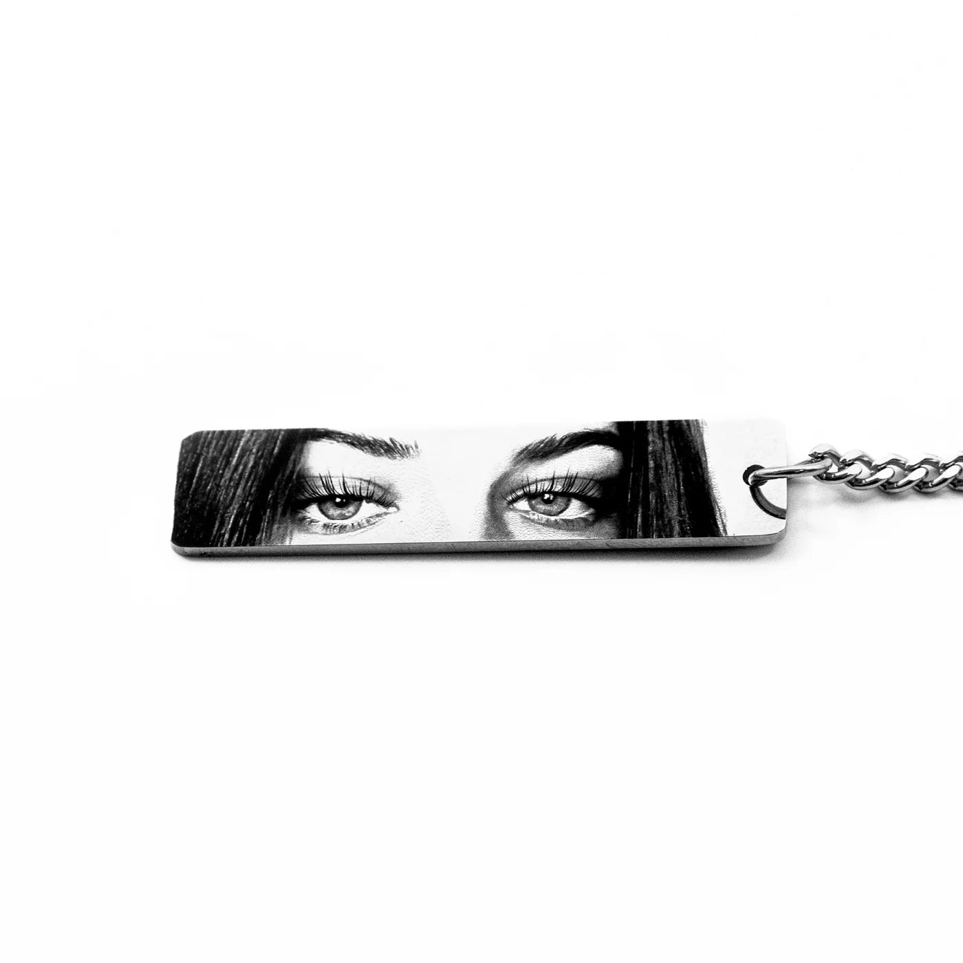 a silver rectangular keychain pendant featuring a young woman's eyes in high contrast black and white