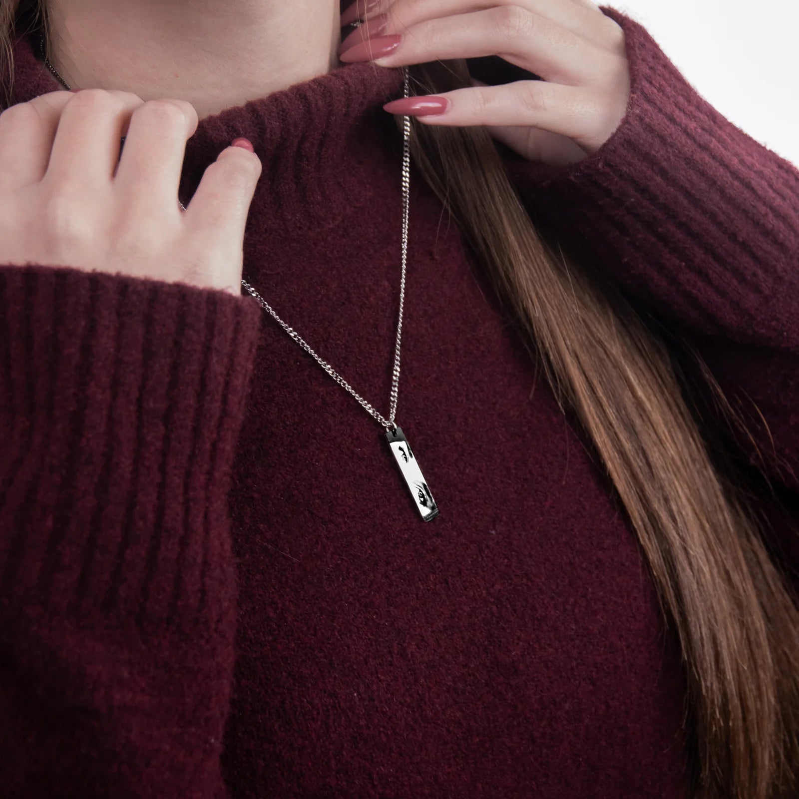 a closeup of a woman in a red sweater wearing a rectangular silver necklace pendant with a printed photo of another young lady's eyes in black and white