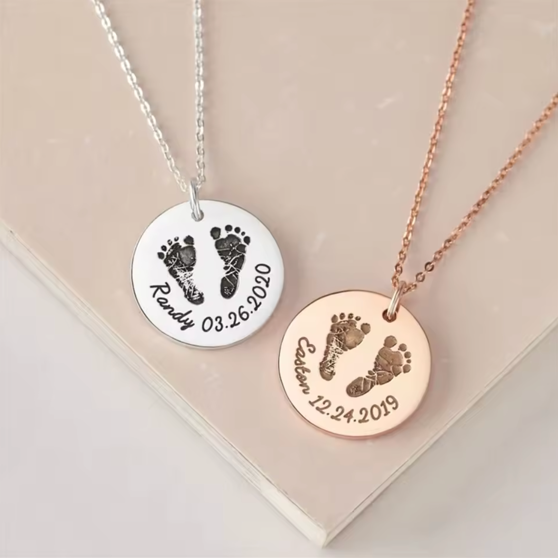 two necklaces, one silver, one rose gold, with circular pendants featuring custom footprints and names with birth dates
