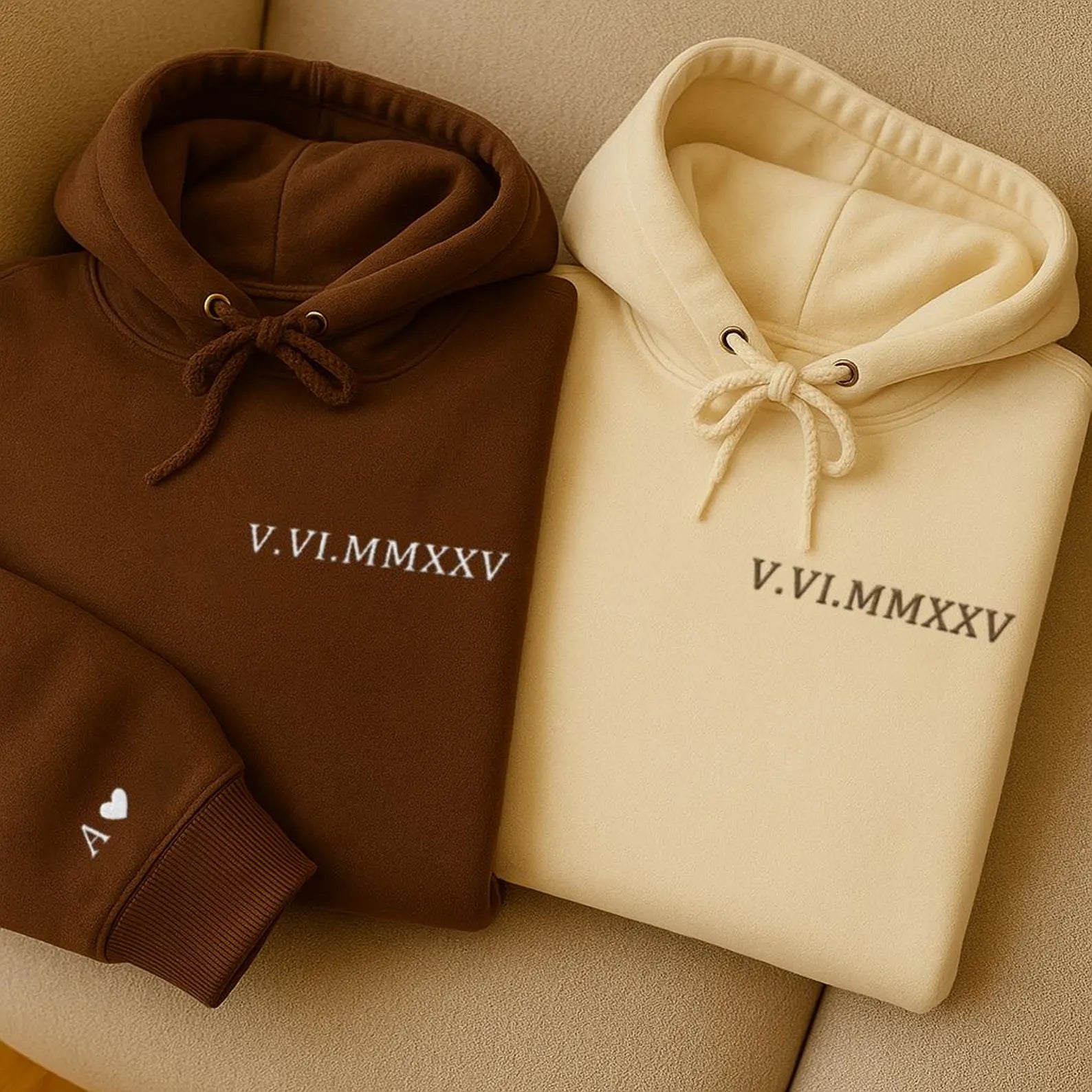 a cream-colored hoodie and a brown hoodie folded neatly together and each featuring the same set of roman numeral embroidery